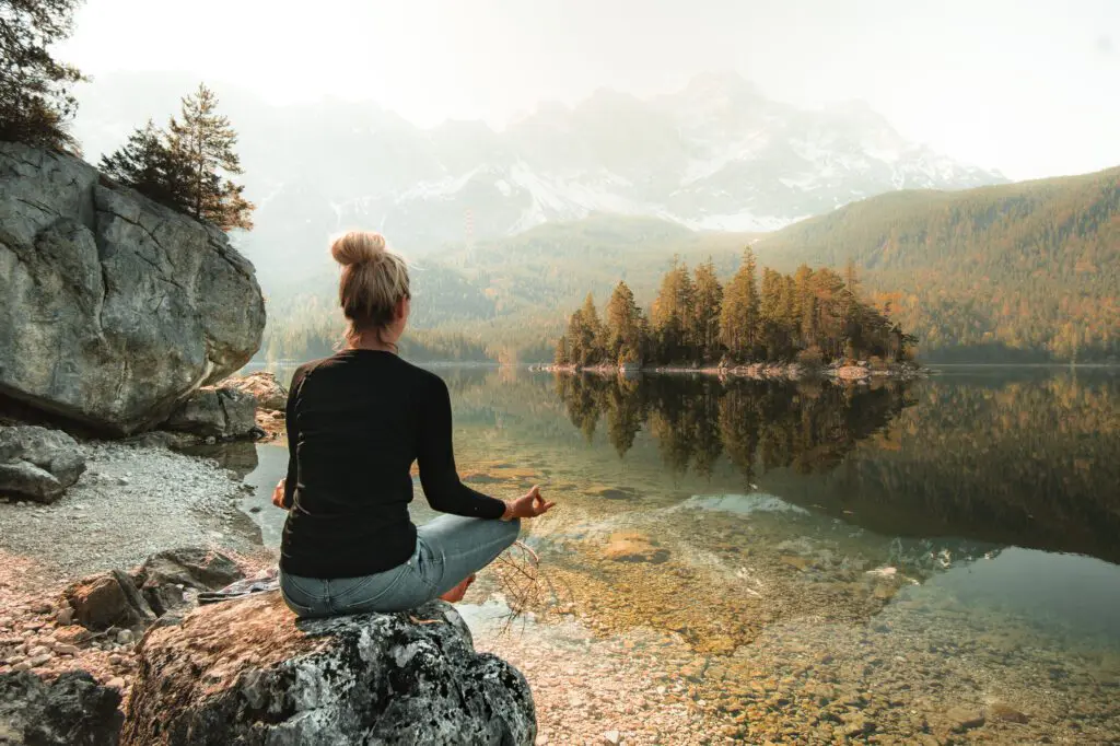 Femme méditant au bord d'un lac paisible avec des montagnes.