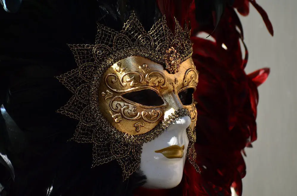 Masque vénitien doré orné de plumes noires et rouges, évoquant l'anonymat du CSE.