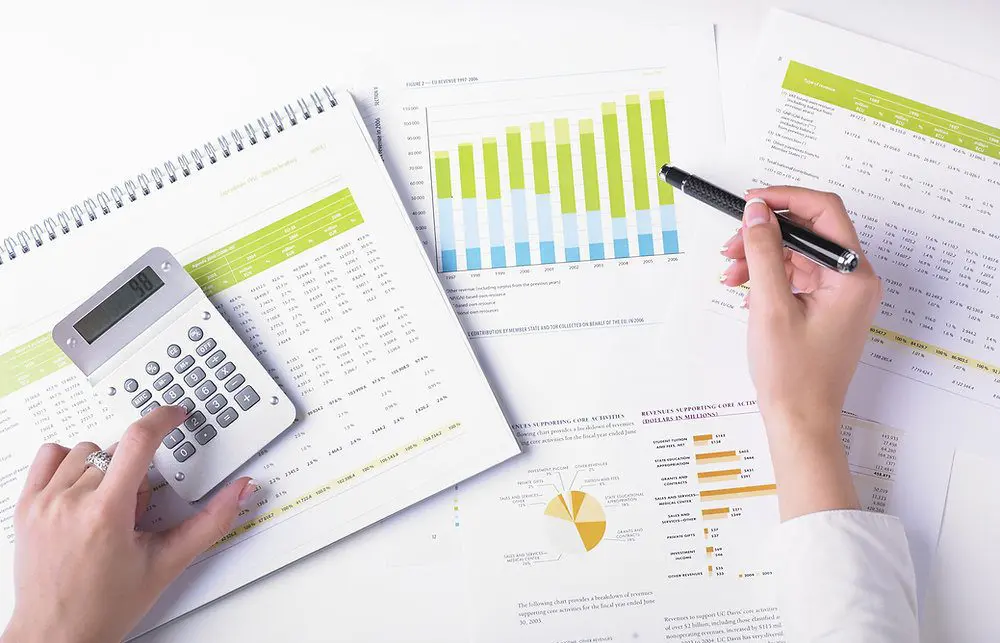 Main d'une personne tenant un stylo au-dessus de graphiques financiers et d'une calculatrice.