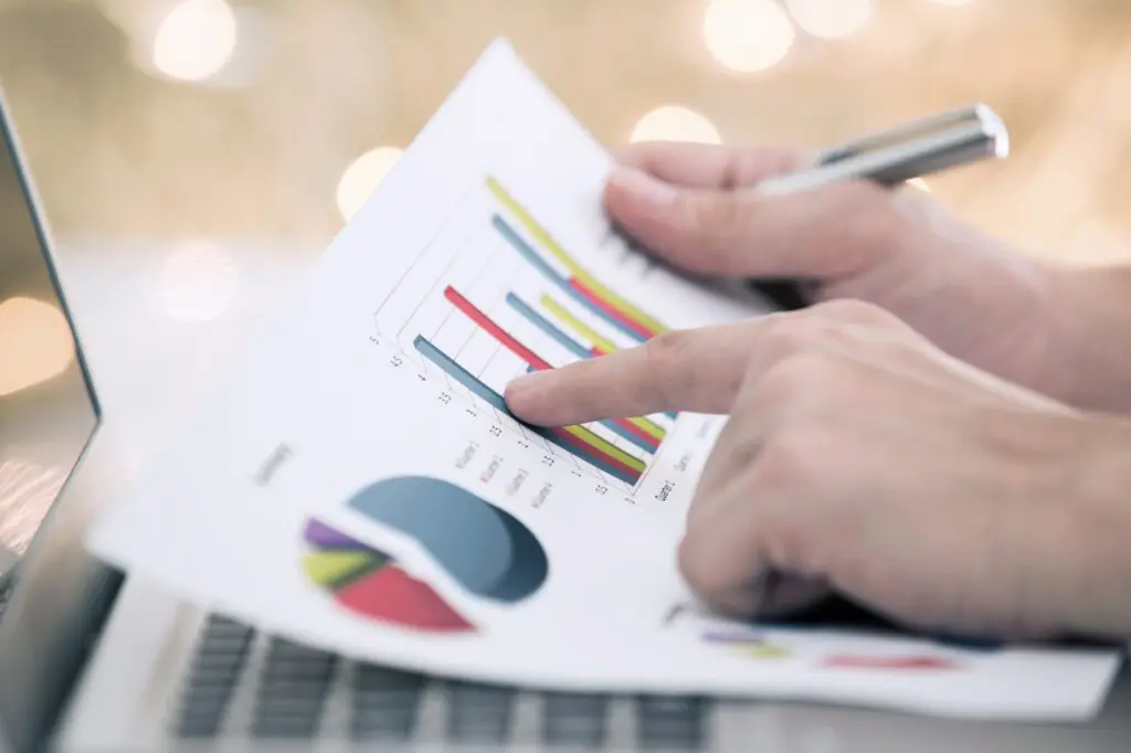 Main d'homme pointant un graphique de données sur un document près d'un ordinateur portable.